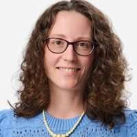 Porträtfoto von Dr. Kathrin Barbe, Brustaufnahme vor neutralem, hellem Hintergrund. Sie trägt einen hellblauen Pullower und blickt freundlich in die Kamera.